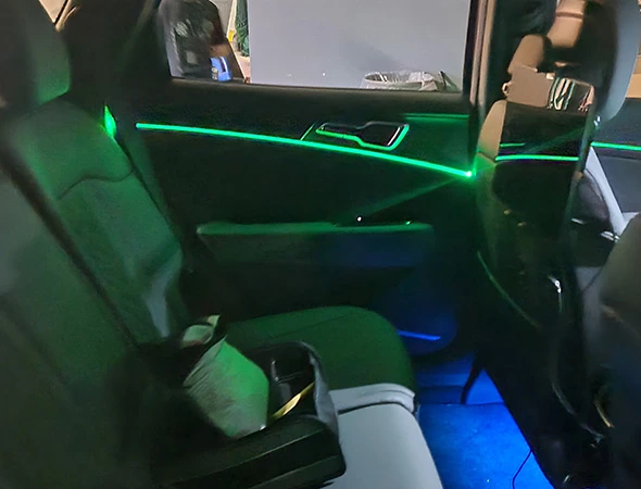 Car interior with ambient green and blue lighting. A rear seat has a console with a cup, creating a sleek and modern atmosphere.