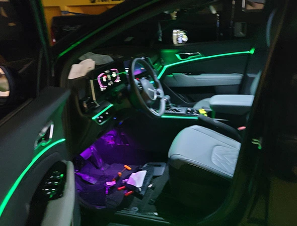 The car interior features green ambient lighting on the dashboard and door panel, with purple lights near the footwell. The atmosphere is modern and tech-focused.