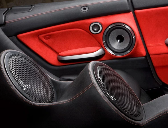 Interior of a car featuring red and black leather upholstery, with prominent speakers on the doors and behind the seats, conveying a sleek, modern vibe.