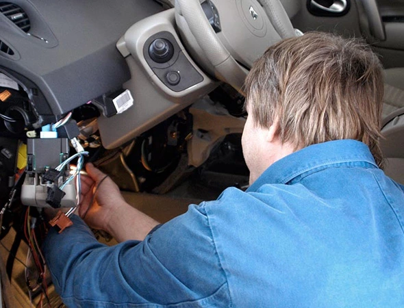 Technician installing car security system under steering wheel