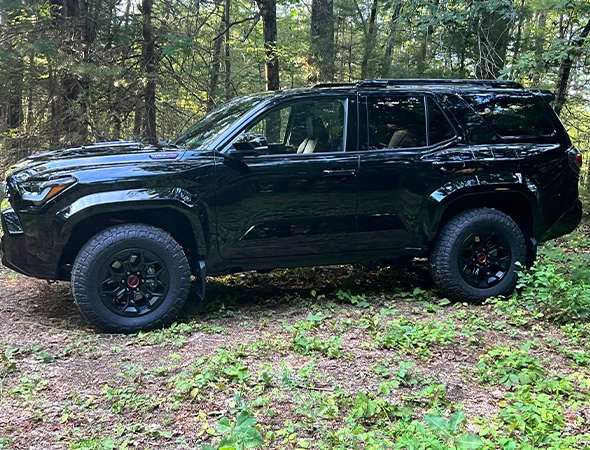 A sleek black SUV is parked in a lush forest setting. The vehicle's rugged tires and glossy finish contrast with the vibrant greenery, conveying adventure and luxury.